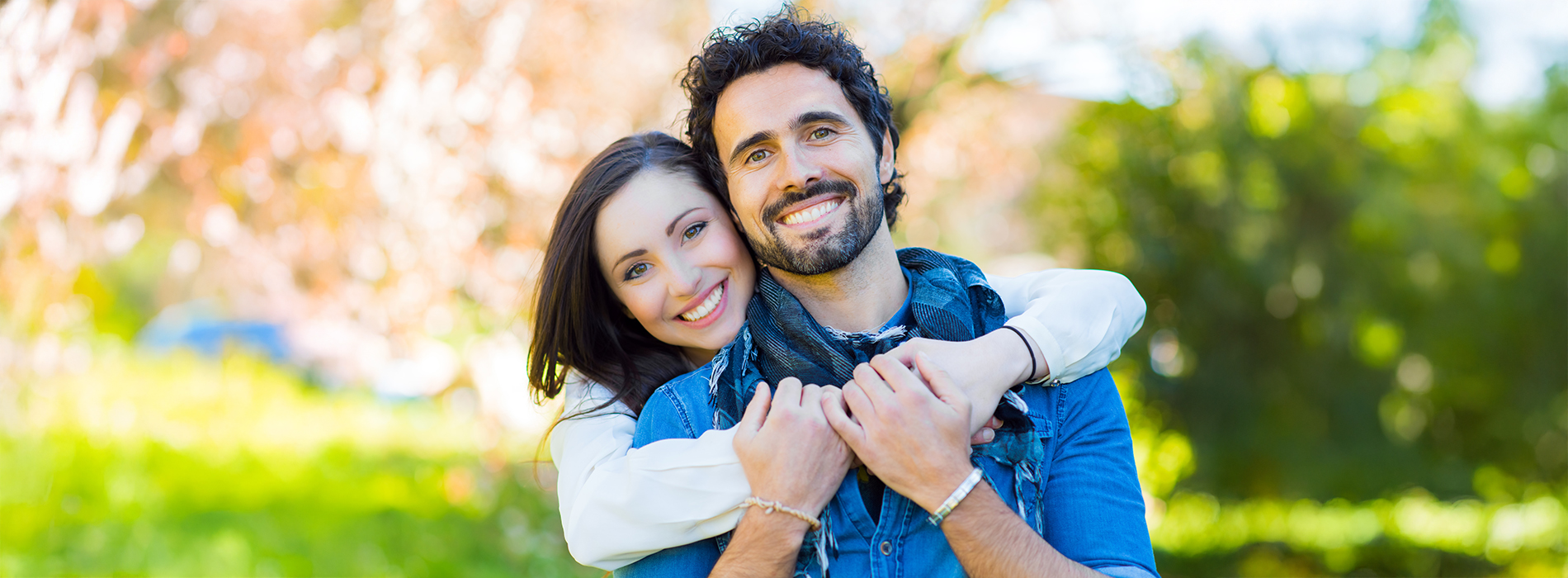 A couple hugging each other outdoors with trees in the background.