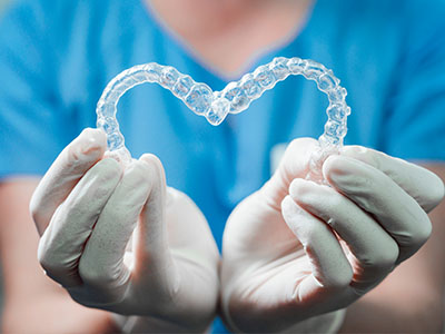 A dental professional s hands holding up a clear orthodontic appliance shaped like a heart.