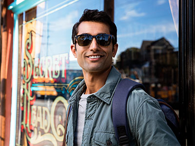 A man wearing sunglasses and a backpack stands outside a storefront with a sign reading  secret life  in the background.