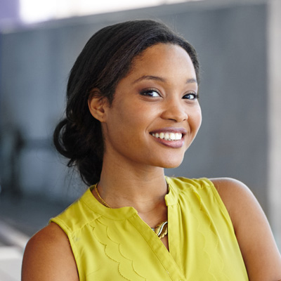 A young woman with a radiant smile poses confidently against a backdrop of a building.