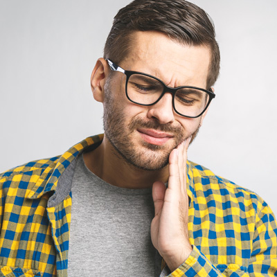 A man with glasses and a plaid shirt is holding his hand to his mouth, possibly in pain or discomfort.