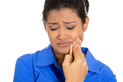 A woman with a concerned expression is holding her hand up to her mouth, possibly brushing her teeth, with a blue shirt visible on her upper body.